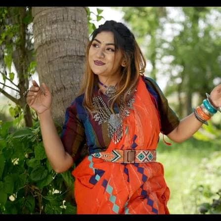 Arpita outdoors beside a palm tree, in a bright orange patterned sari and a silver collar