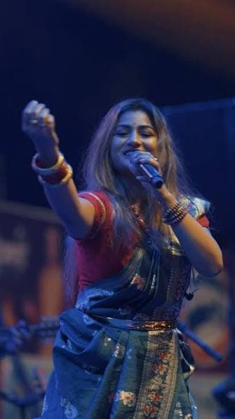 Arpita full length on a concert stage, one arm raised as she sings