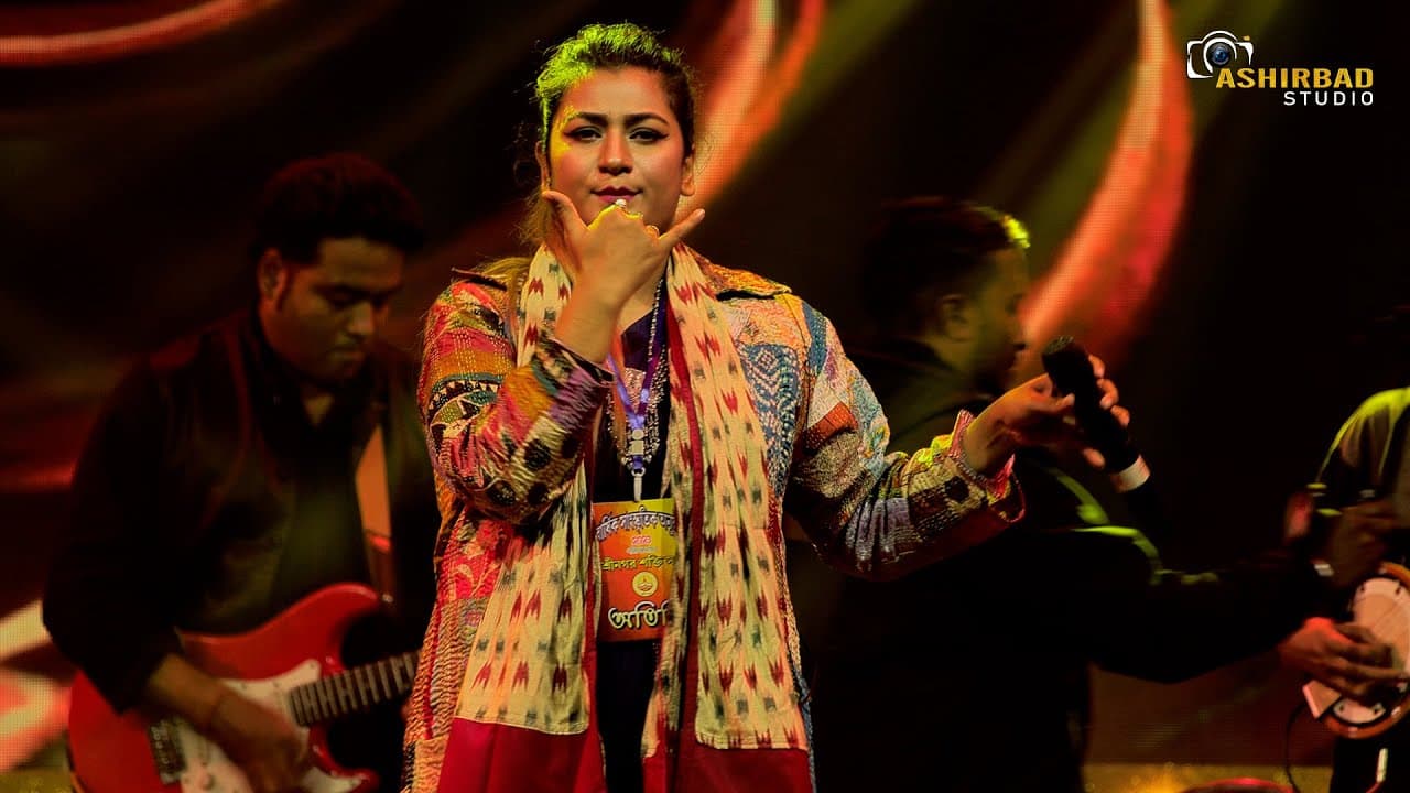 Arpita performing with her band in a patchwork jacket, guitarist and singers behind her