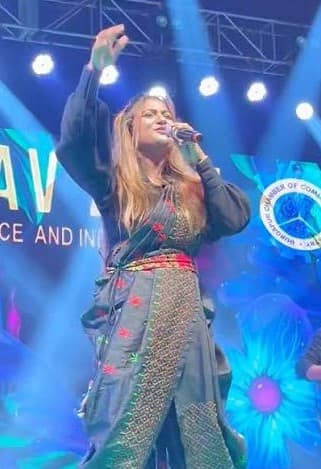 Arpita on a festival stage under blue lights, arm raised to the crowd